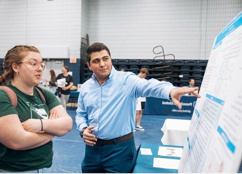 A student points to his research poster board, explaining its contents to an interested visitor.